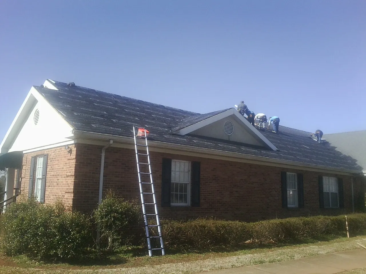 Crew tearing shingles off a brick ranch roof with a ladder set — Metal Roof Repair work by our crew in Terrace Park