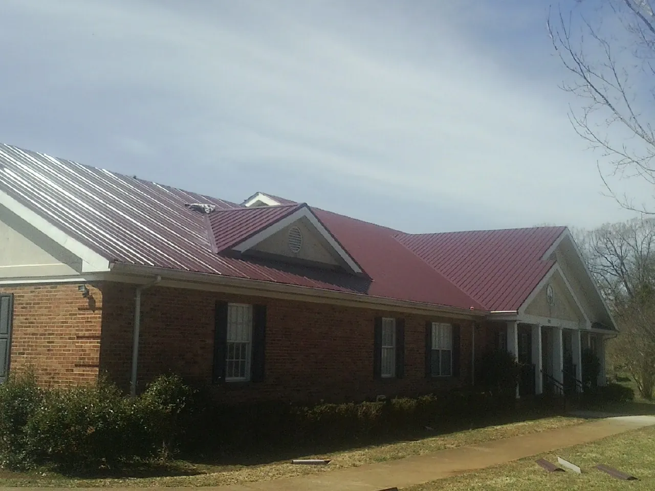Red metal roof with gabled entries on a long brick building, from a Hail Damage Roof Repair job in Terrace Park