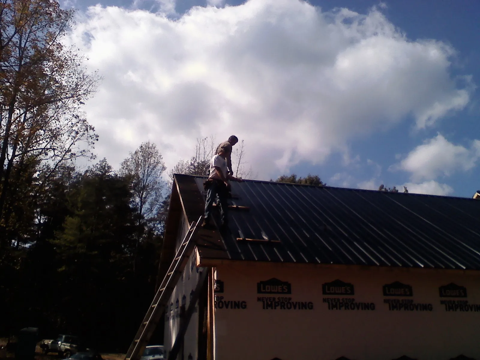 Roofer fastening dark metal panels high against a cloudy sky, from a Roof Inspection job in Terrace Park