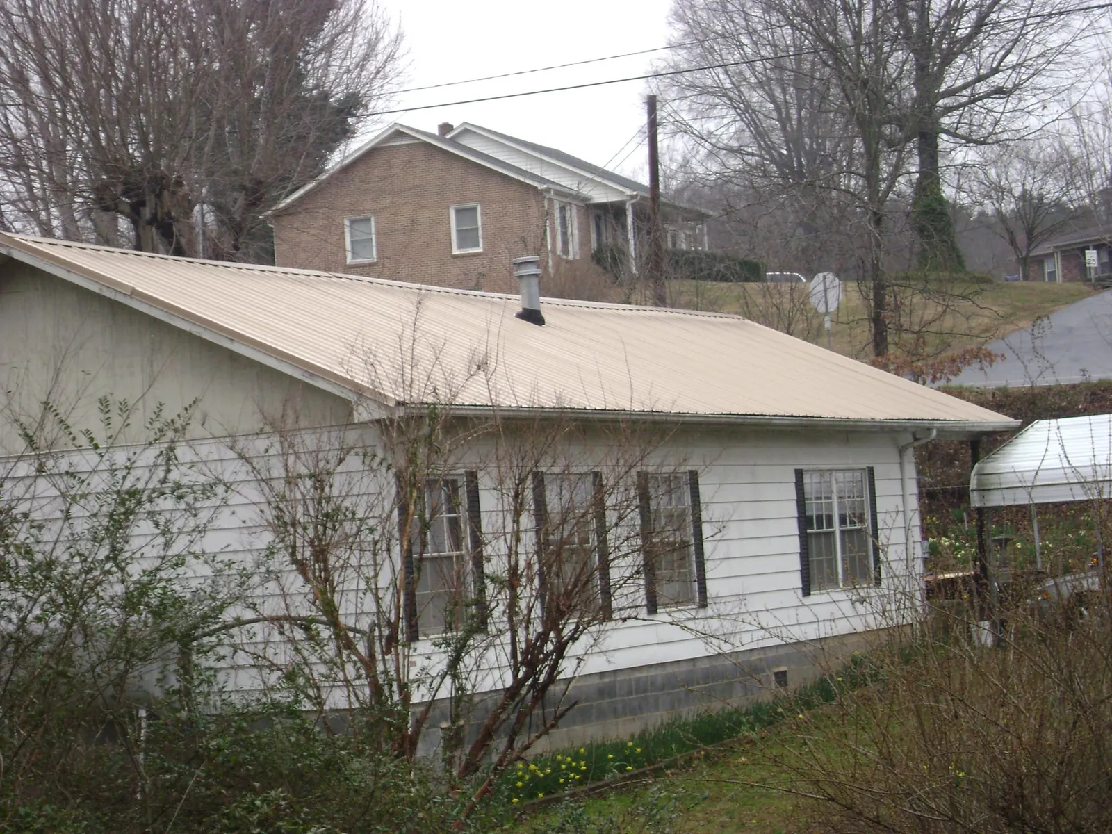 Tan metal roof on a white sided house set into a hillside — Commercial Roofing by Roofing Brothers in Terrace Park